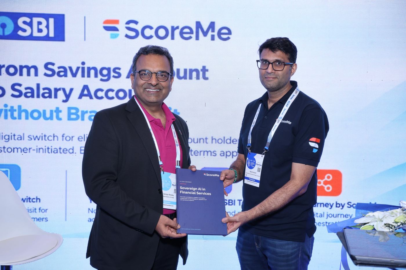 Two people holding a copy of the report in front of an SBI and ScoreMe screen.
